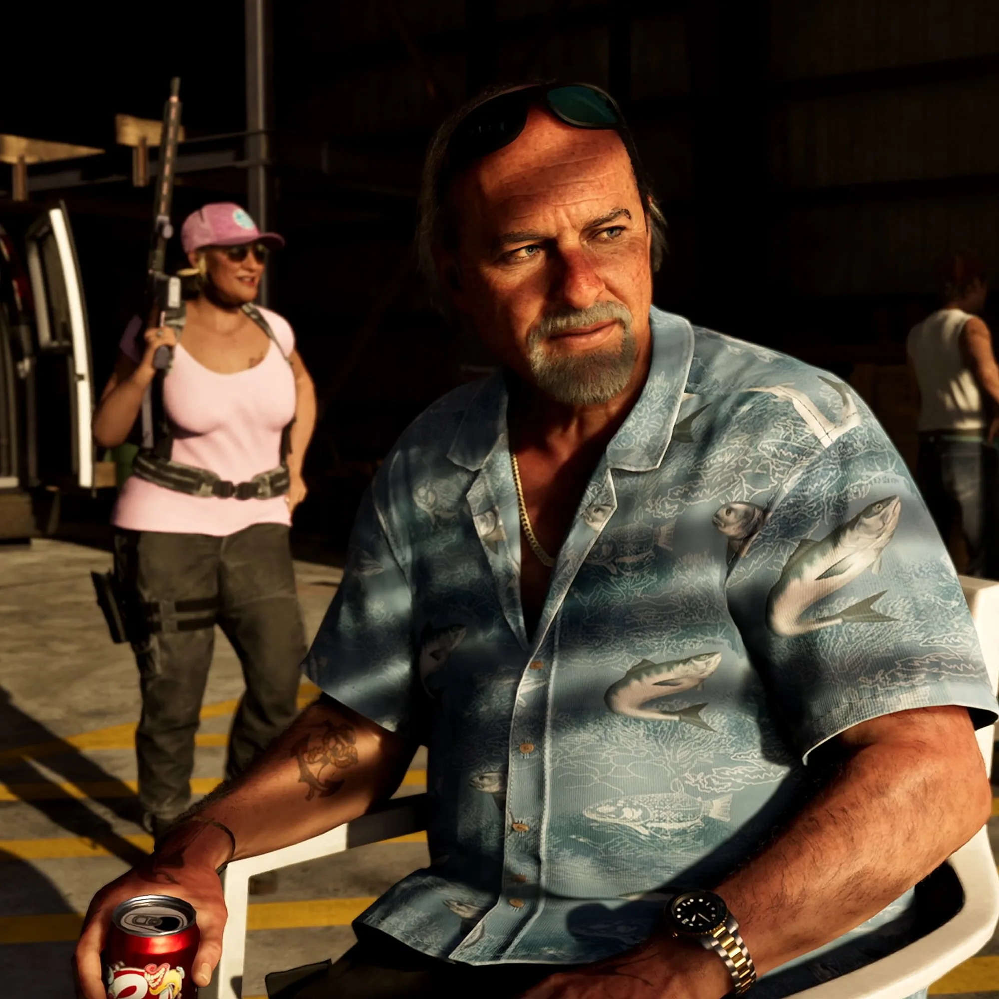 A bearded man in a blue patterned Hawaiian shirt holds a drinks can on a night-time dock, with a woman holding a rifle and film lighting equipment behind him.