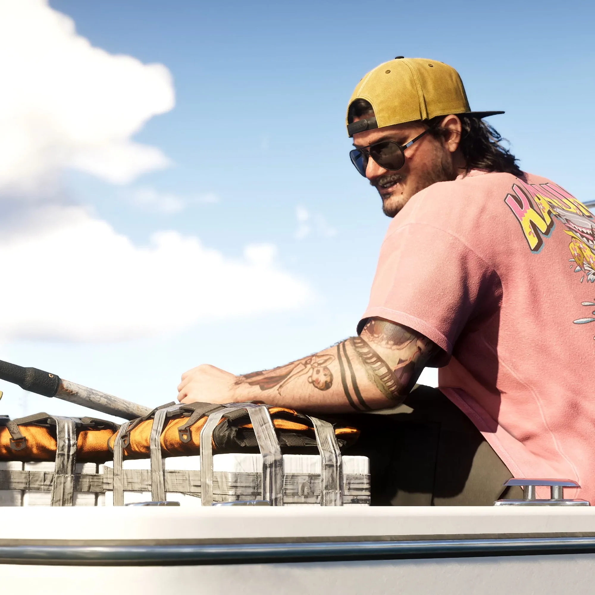 A man in a yellow cap, dark sunglasses and a pink graphic T-shirt smiles from the deck of a boat on open water under a blue sky.