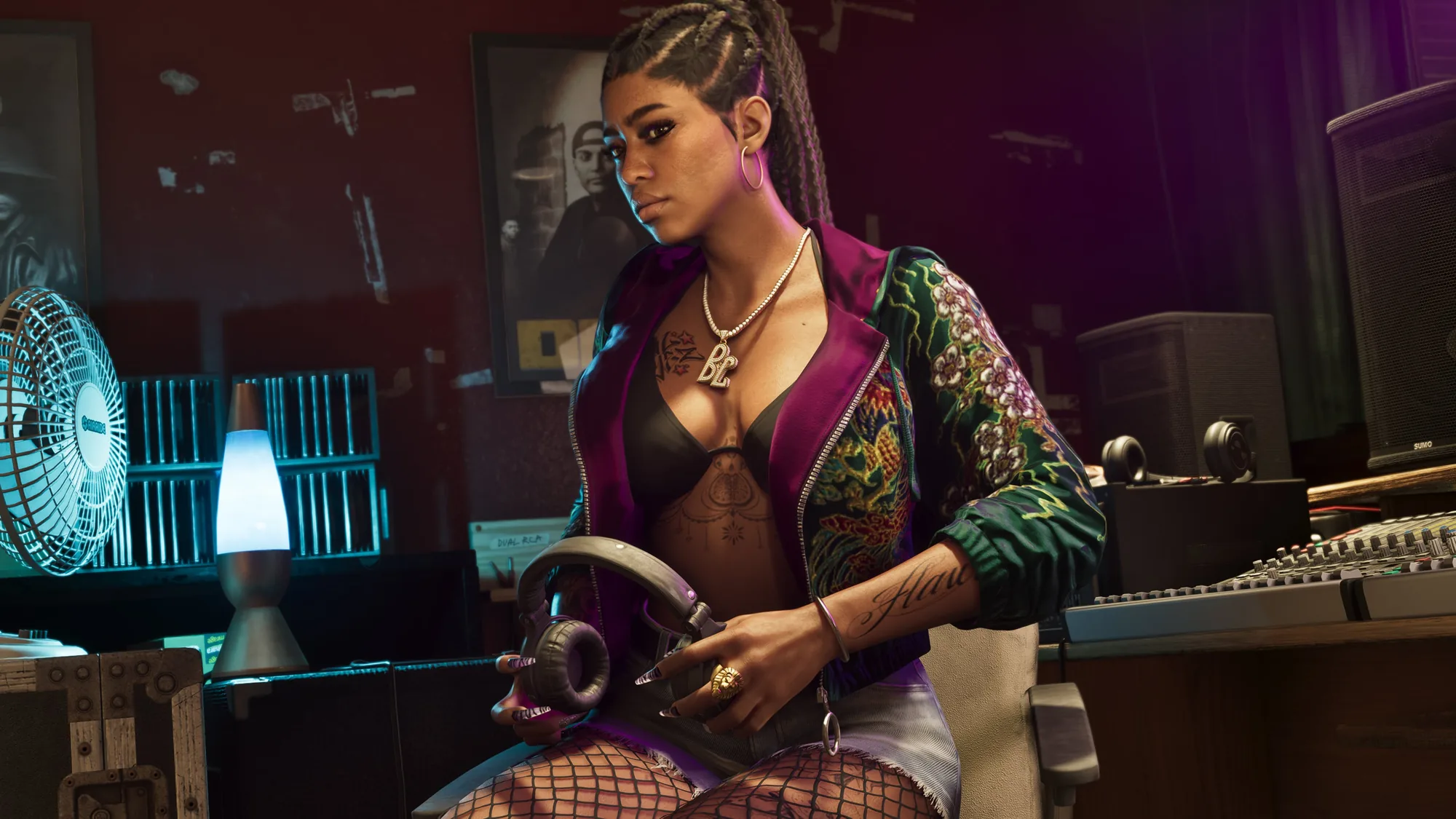 A woman in a patterned jacket, jewellery and tattoos sits at a music production desk surrounded by studio equipment under cool blue and magenta lighting.