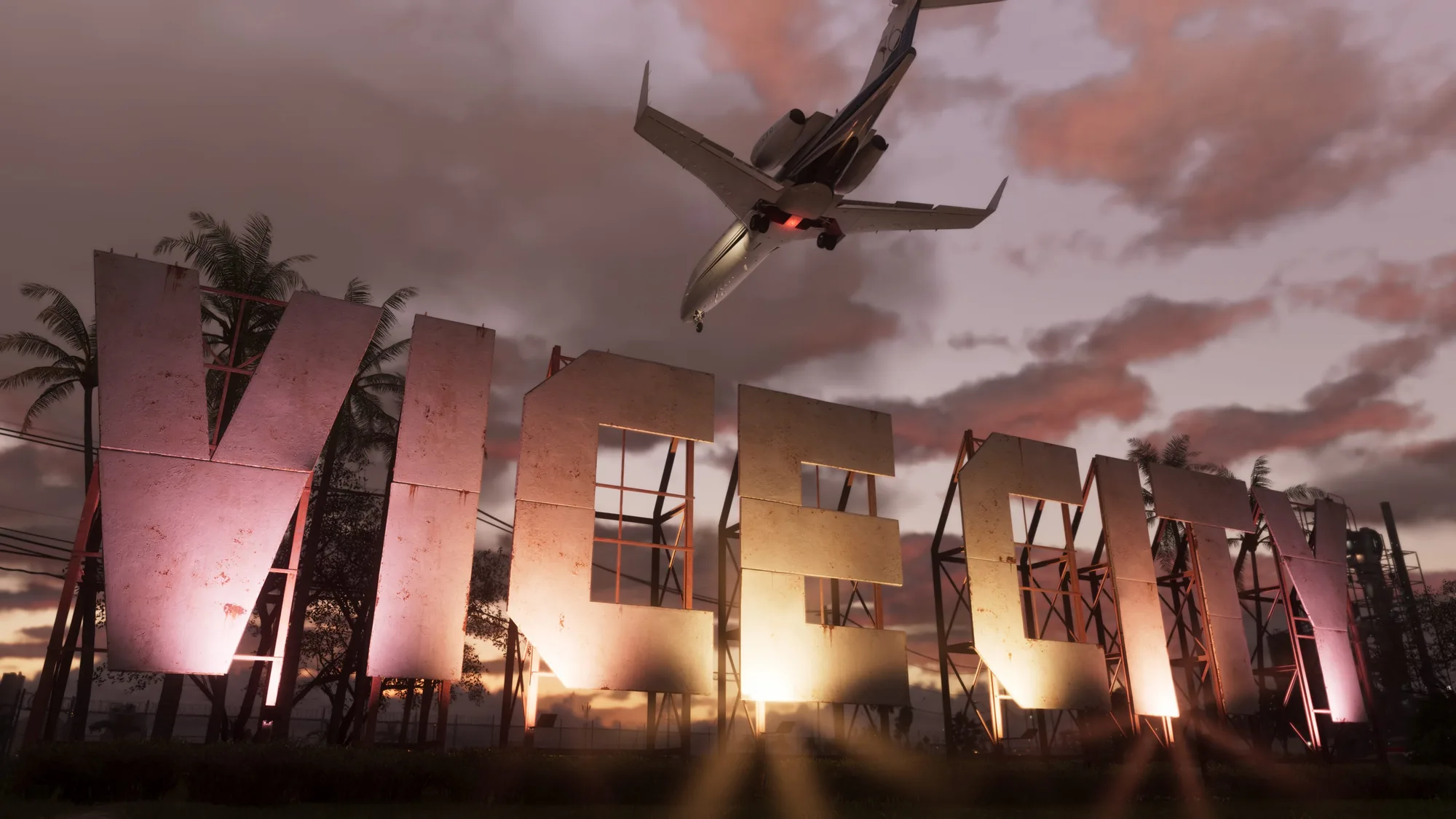 A military-style aircraft with its landing gear down flies low over an industrial district at dusk, passing illuminated pink and gold billboards against a sunset sky with palm trees.