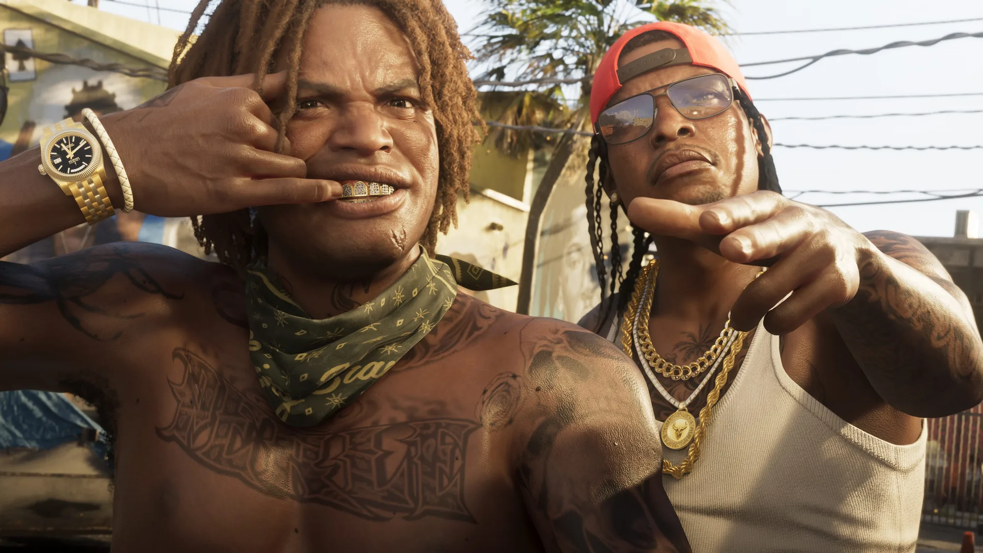 Two tattooed men in gold jewellery, chains and caps pose for the camera on a residential street in bright daylight, with palm trees, power lines and low buildings behind them.